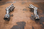 A wide view of two Valvetronic Designs Free Flow Headers (for Audi R8 V10 / Lamborghini Gallardo LP / Lamborghini Huracan) exhaust pipes on the ground. 