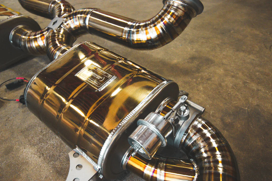 A close up of Valvetronic Designs gold Valved Sport Exhaust System (for Audi R8 V10 Gen 2 2017+)  with wires on the ground.