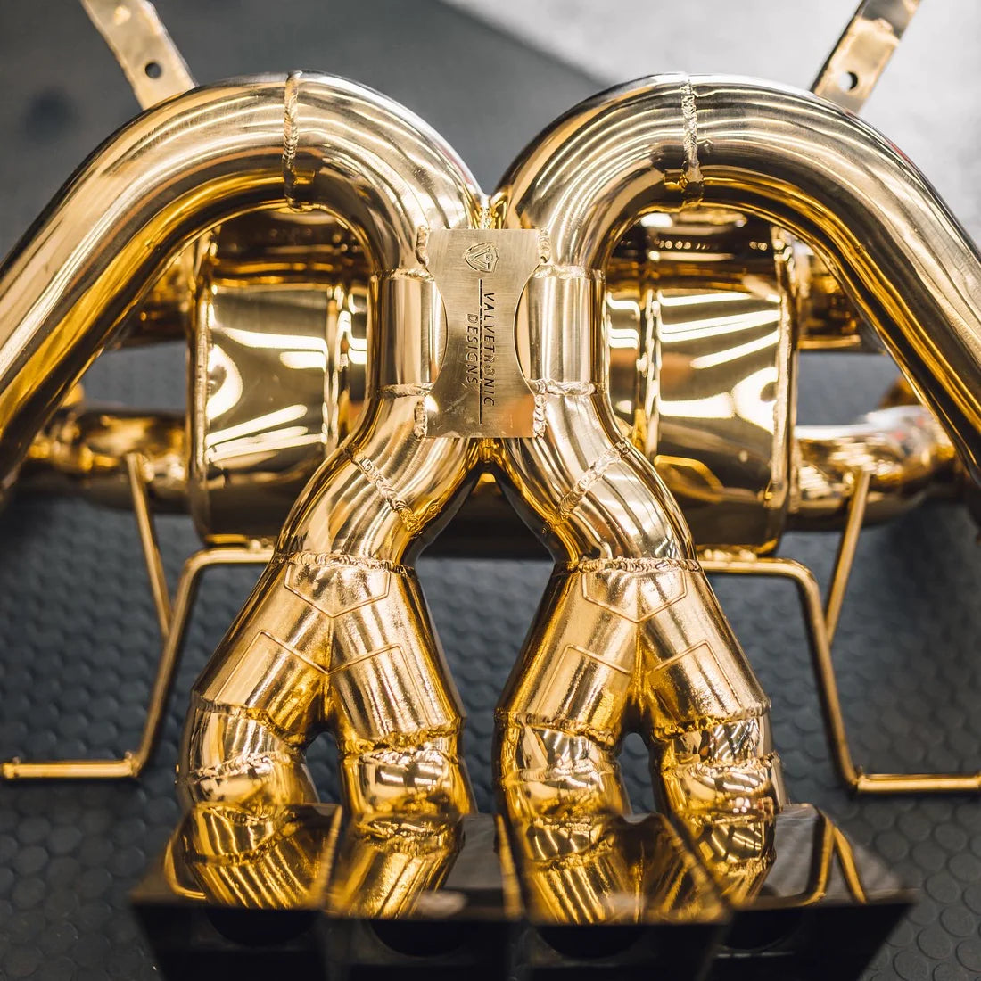 A close up of Valvetronic Designs Valved Sport Exhaust System on a grey carpet on the ground (for Lamborghini Aventador LP700 / SV).