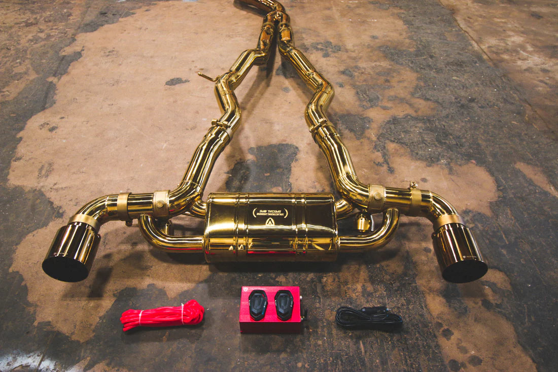 A close view of Valvetronic Designs Anodized Gold Valved Sport Exhaust System with valve controller and wires on the ground (for Toyota Supra A90 / A91).