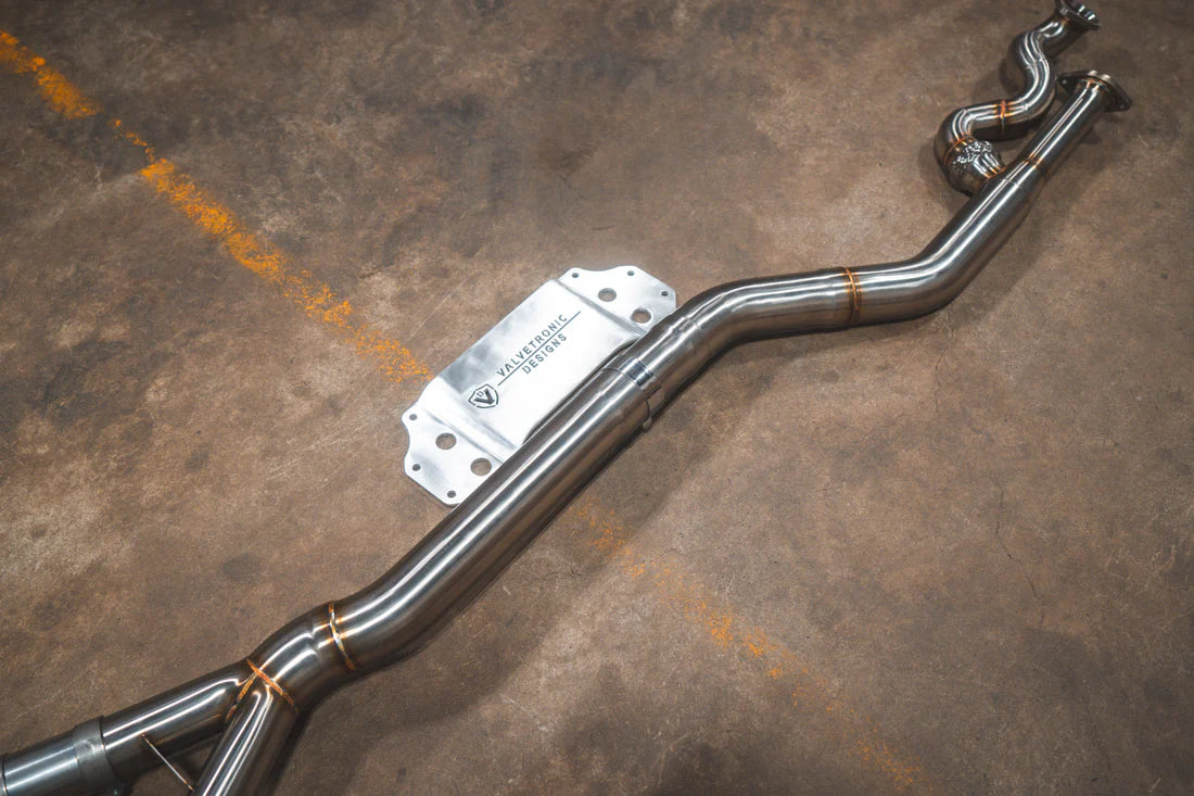 A side overview of Valvetronic Designs Equal Length Midpipe in Brushed Stainless Steel on the ground (for BMW G8x M3 / M4).