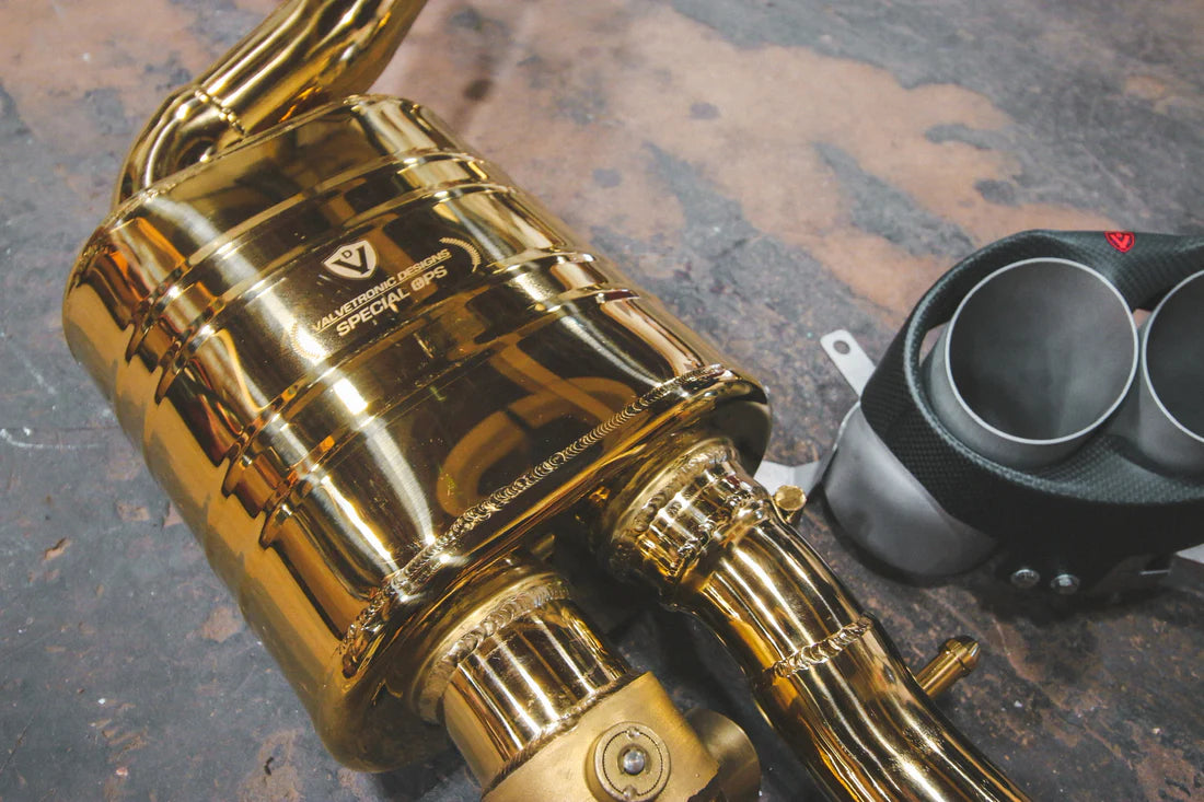 A close up of parts of Valvetronic Designs gold Valved Sport Exhaust Sytem with the brand's logo (for Audi RS6 / RS7 C7) on the ground.