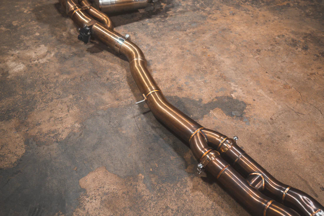 A wide view of Valvetronic Designs Equal Length Valved Sport Exhaust System's pipes on the ground (for BMW M3 F80, M4 F82, M4 F83).