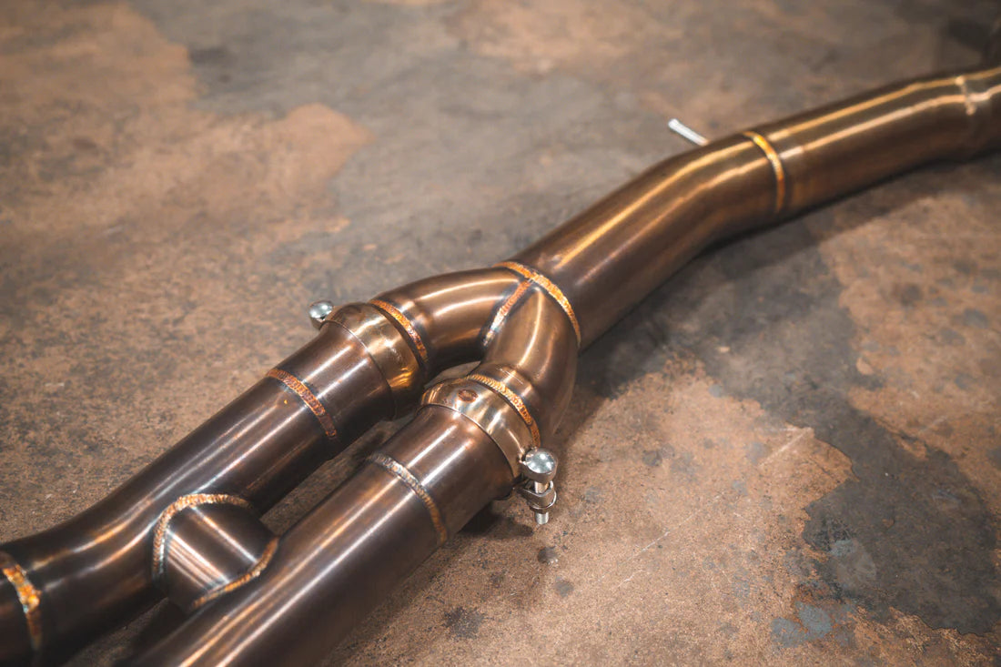 A close up view of Valvetronic Designs Equal Length Valved Sport Exhaust System's pipes on the ground (for BMW M3 F80, M4 F82, M4 F83).