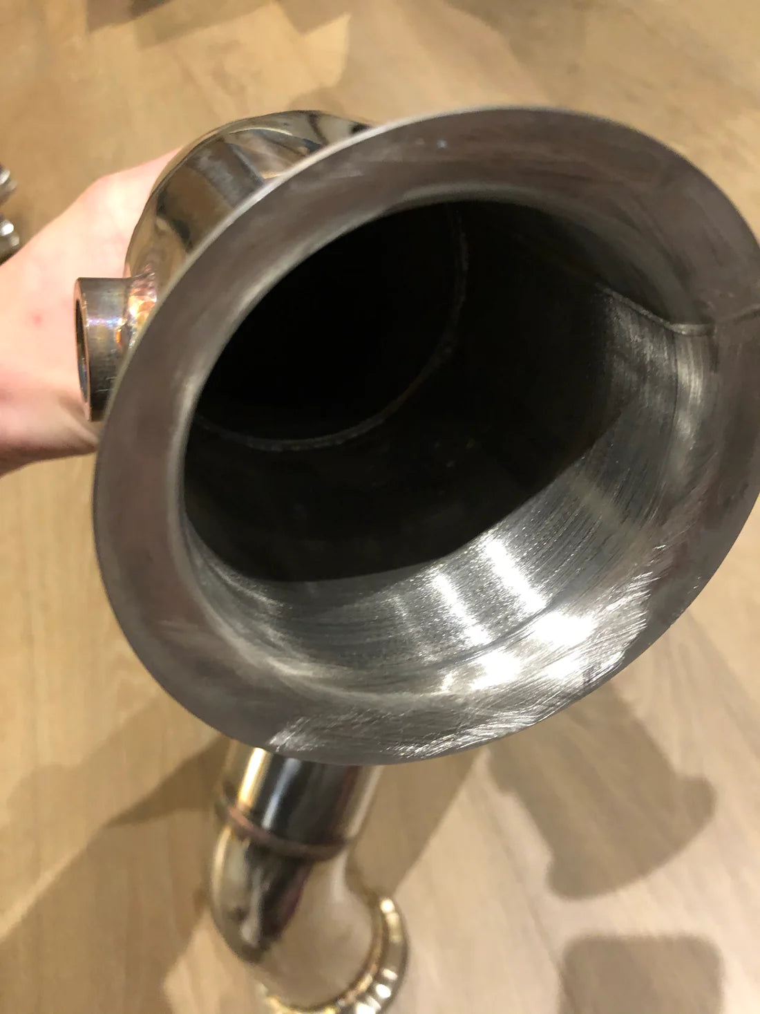 A close up view of Valvetronic Designs Free Flow Front Pipe being held by a hand on a wooden floor (for Mercedes AMG GT/ GTC / GTR).