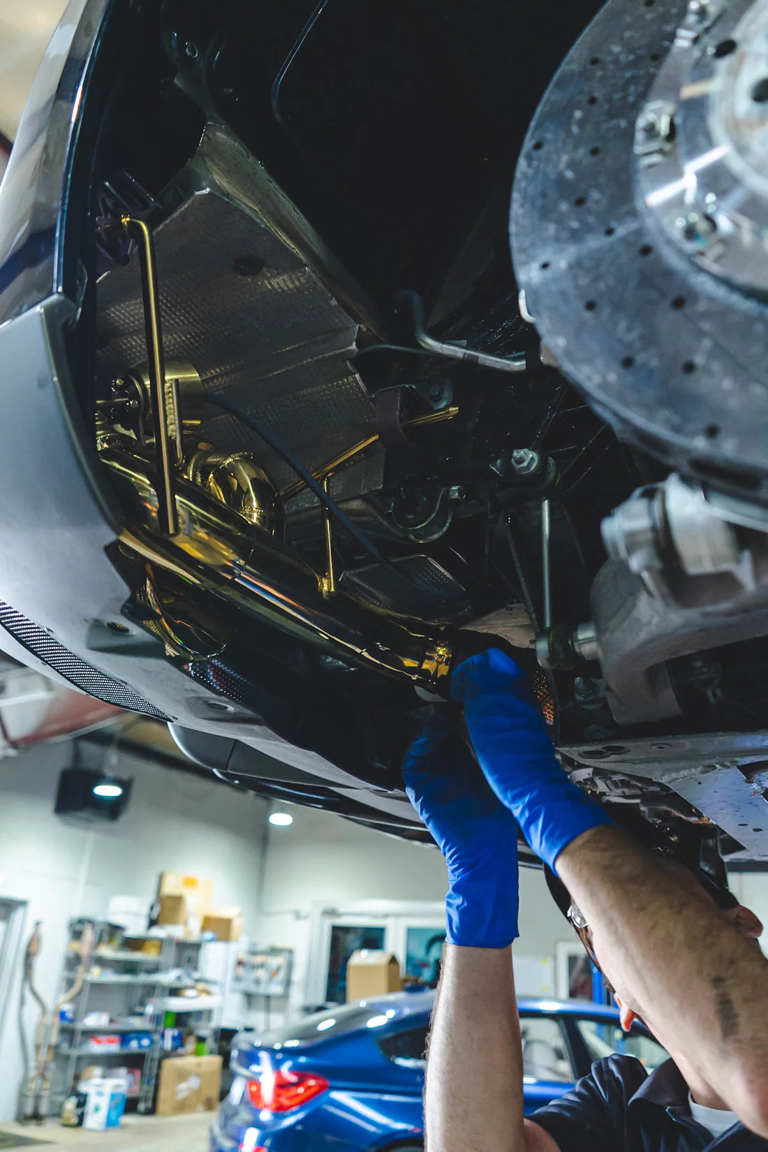 A close view of a man fitting Valvetronic Designs Valved Sport Exhaust System on a lifted car (for Ferrari F12 / 812).