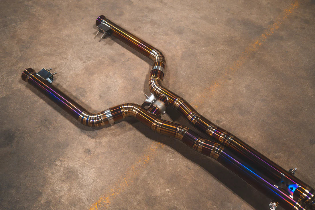 A side overview of Valvetronic Designs Titanium Valved Sport Exhaust System's pipes on the ground (for Mercedes W205 C63 / C63s).