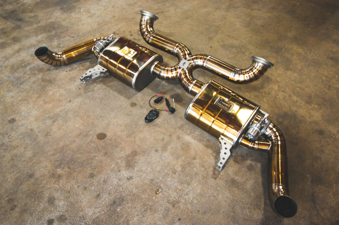 A wide angle view Valvetronic Designs gold Valved Sport Exhaust System (for Audi R8 V10 Gen 2 2017+)  with wires on the ground.