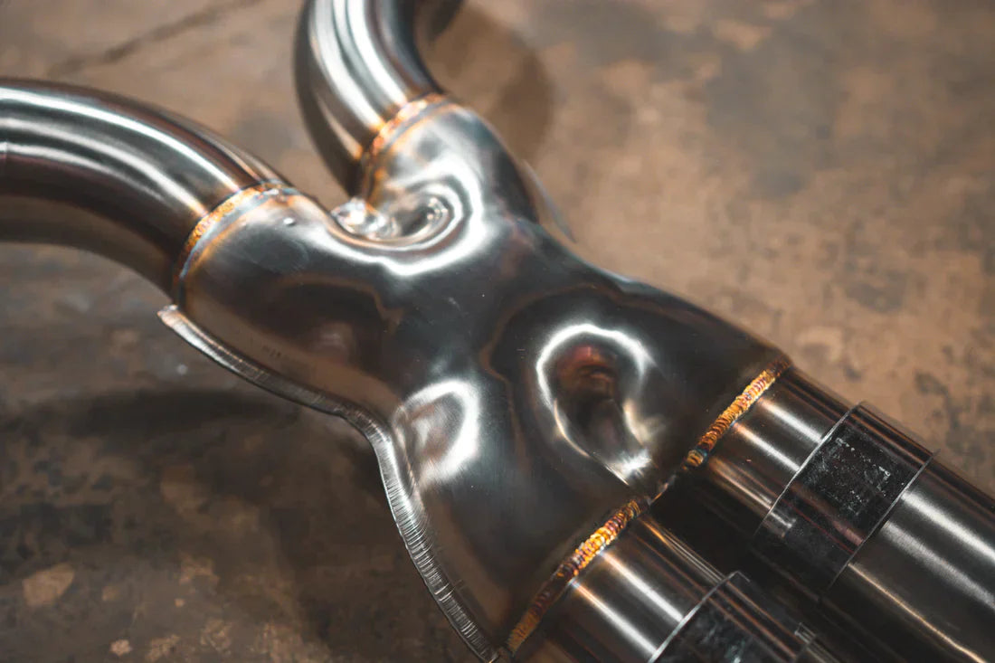 A close view of Valvetronic Designs Valved Sport Exhaust System's pipes on the ground (for BMW F90 M5). 