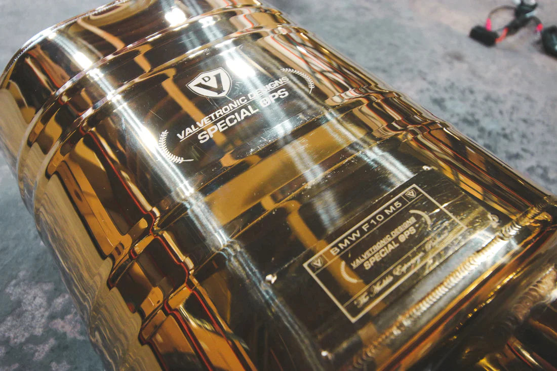 A wide overview of Valvetronic Designs Anodized Gold Valved Sport Exhaust System's muffler on the ground (for BMW F10 M5 / F12 M6 / F06 M6)
