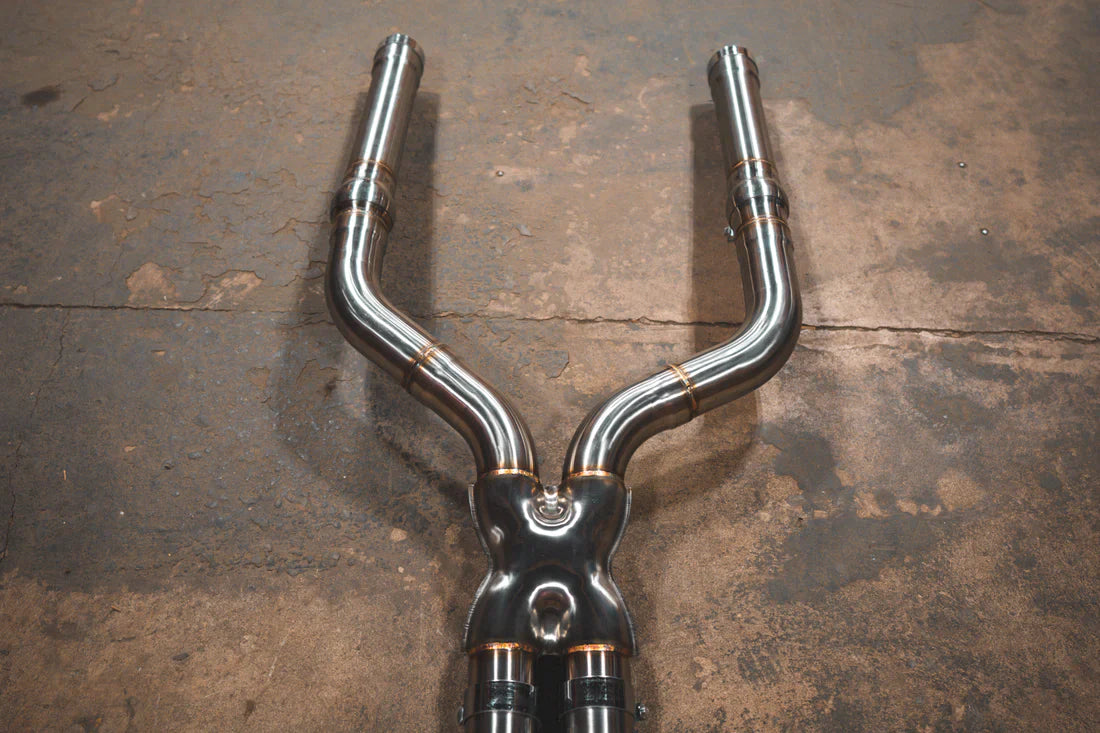 A close view of Valvetronic Designs Valved Sport Exhaust System's pipes on the ground (for BMW F90 M5). 