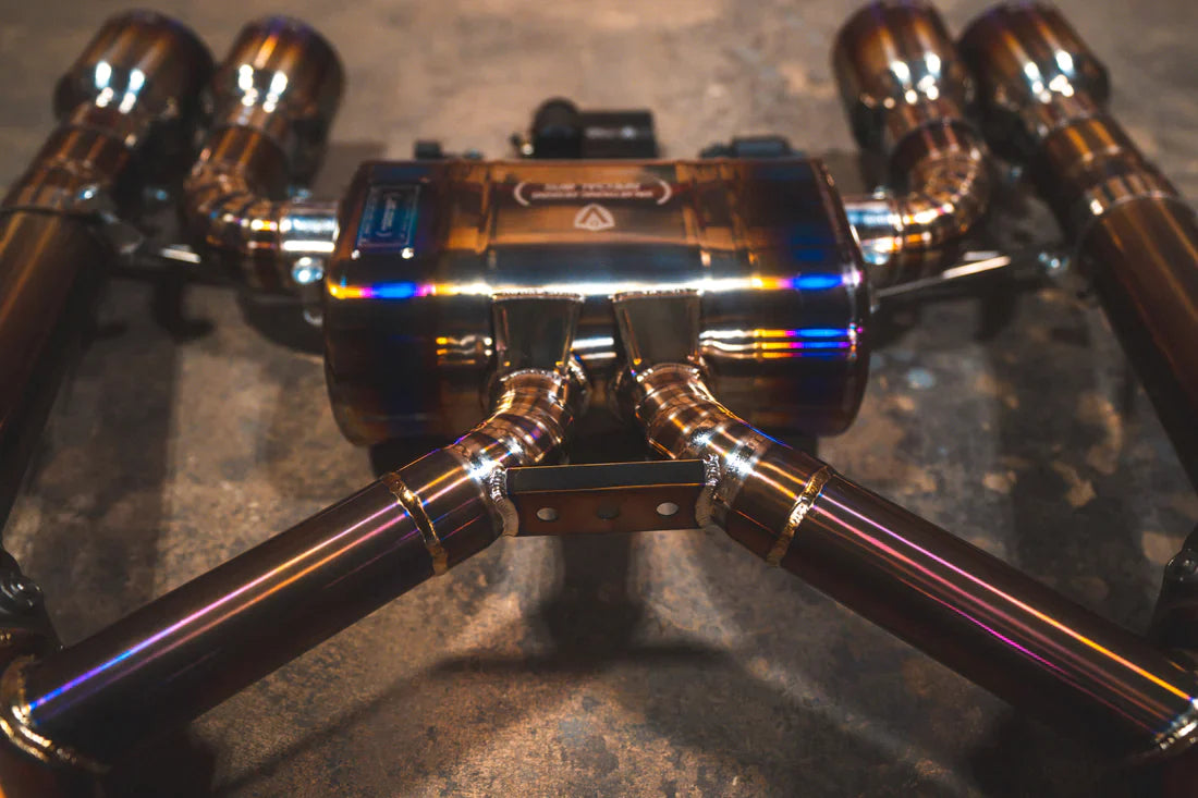 A close view of Valvetronic Designs GRADE 5 TITANIUM Valved Sport Exhaust System with Raw Titanium Burnt exhaust tips on the ground (for BMW G8x M3 / M4).