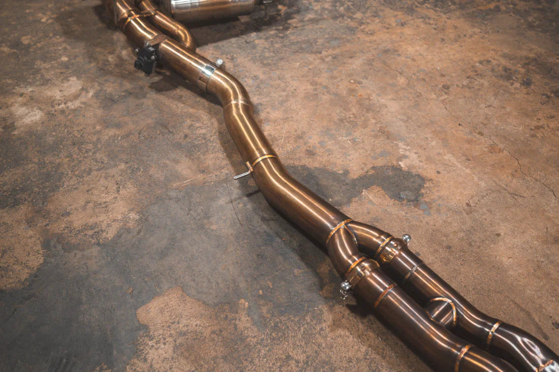 A wide view of Valvetronic Designs Equal Length Valved Sport Exhaust System's pipes on the ground (for BMW M3 F80, M4 F82, M4 F83).