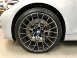 A close up view of a white BMW car with the front wheel fitted with AP Racing by Essex Radi-CAL ENP Competition Brake Kit (Front CP9660/372mm)- BMW F87 M2 & M2 Competition, F80 M3, F82 M4