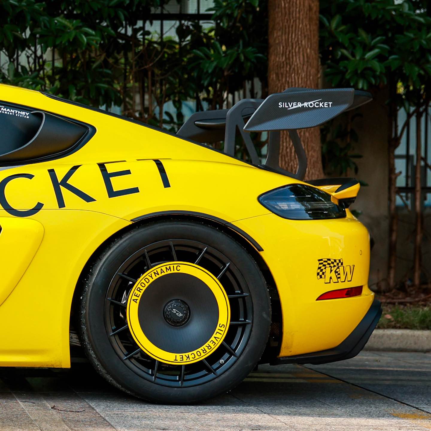 a side view of yellow Porsche gt4rs with silver rocket carbon wing with decals