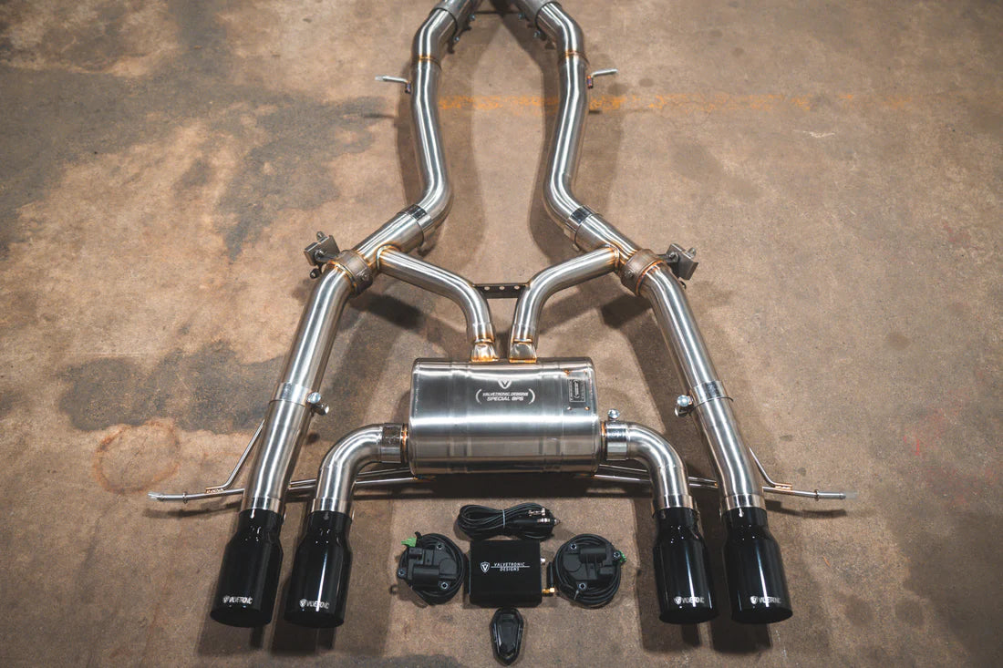 A close view of Valvetronic Designs Axleback Valved Sport Exhaust System with Black exhaust tips on the ground (for BMW G8x M3 / M4).