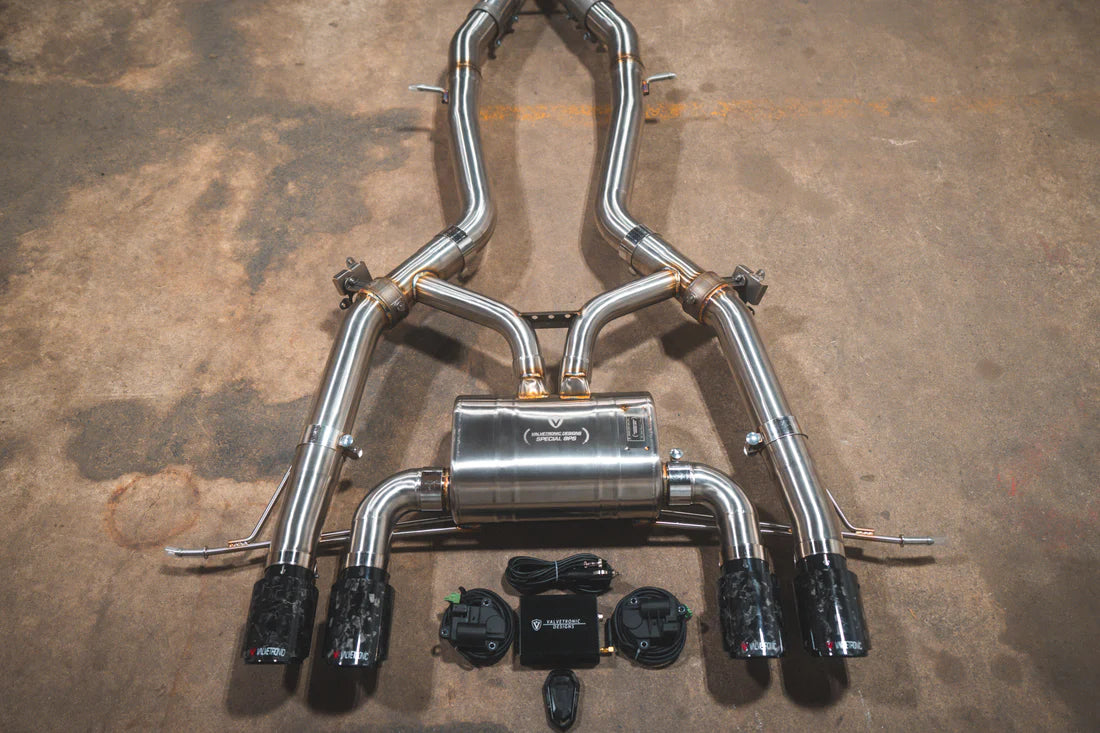 A close view of Valvetronic Designs Axleback Valved Sport Exhaust System with Forged Carbon Fiber exhaust tips on the ground (for BMW G8x M3 / M4).