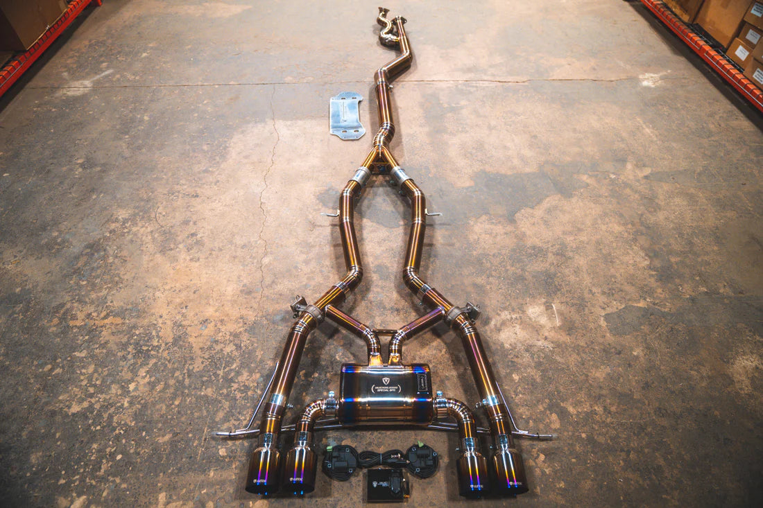 A top overview of Valvetronic Designs Catback GRADE 5 TITANIUM Valved Sport Exhaust System with Raw Titanium Burnt exhaust tips on the ground (for BMW G8x M3 / M4).